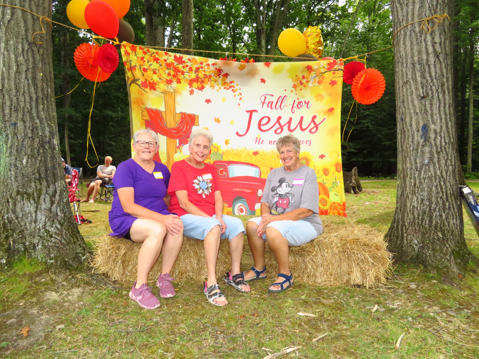 Three ladies posing on hay bales at the Fall for Jesus backdrop