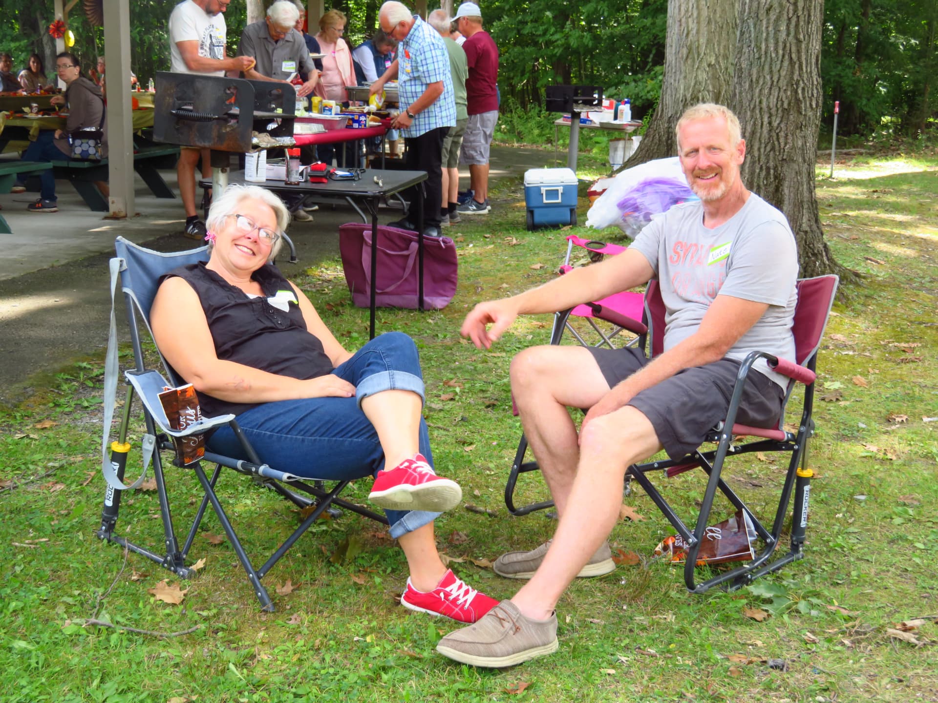 Two members relaxing in lawn chairs near the grills
