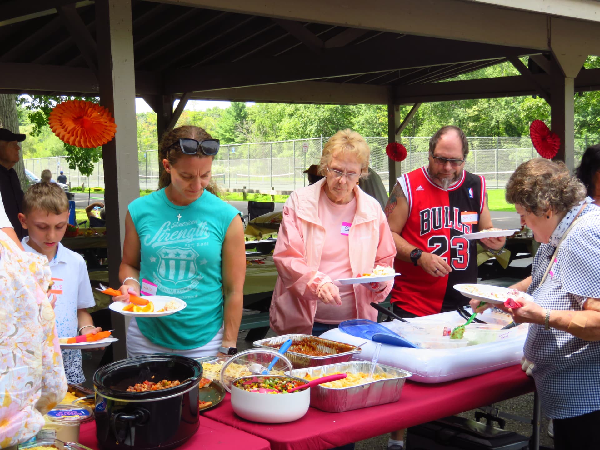 Members filling their plates from casseroles and salads under the pavilion